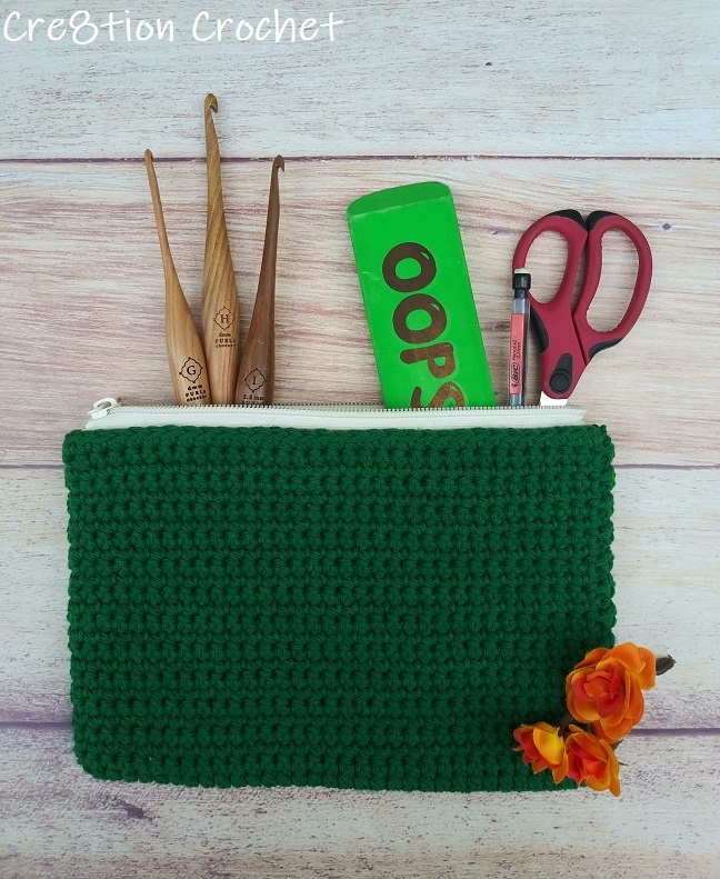 Dark green crochet cosmetic bag with crochet hooks, scissors, and a green case on top.