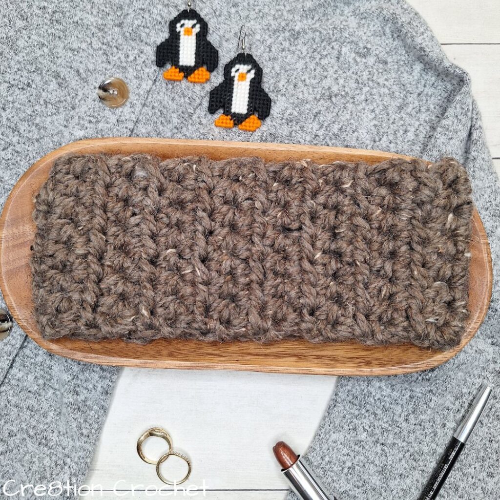 Thick brown super bulky crochet ear warmer on a wooden tray.